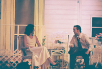 A young man talking with a young woman, both sitting outside a house