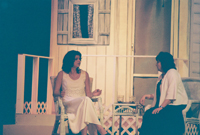 A younger woman talking with an older woman, both sitting in front of a house