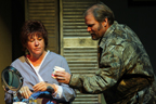 A woman in a blue robe at a make-up table, and a man in a camouflage jacket