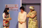 Three women talking, one in a short skirt, one in a long beige dress, one in a floral print dress