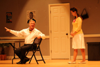 A sitting man in a white shirt talking to a standing woman in a yellow sweater