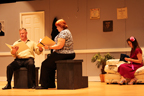 A sitting man and woman reading from scripts while another woman knits