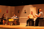 A sitting man and woman reading from scripts while another man and woman sit at a table