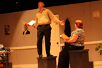 A man standing on a block and a woman sitting on a block, both reading scripts 