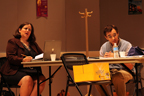 A man and a woman sitting at a table, the woman talking, the man hunched over