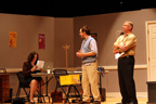 Two men standing, with another woman sitting at a table