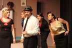 A man in a hat and tie talking, with three women behind him listening and another standing to his right