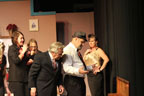 Two women in pansuits, a man in a suit, a man in a hat and tie, and a woman in a gold lame top