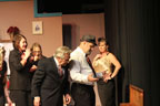 Two women in pansuits, a man in a suit, a man in a hat and tie, and a woman in a gold lame top