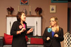 Two women wearing black pantsuits talking in front of a fireplace