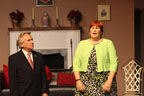 A man in a suit and a woman in a greet sweater talking in front of a fireplace