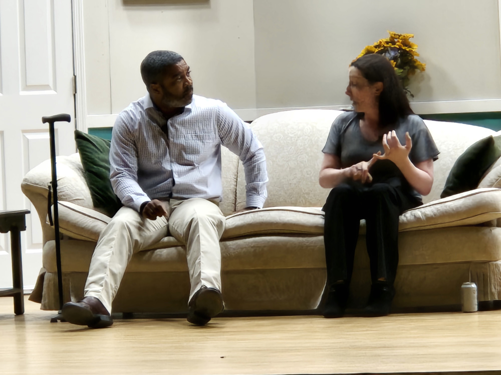 A man and a woman sitting on a couch, the man has a black cane next to him.