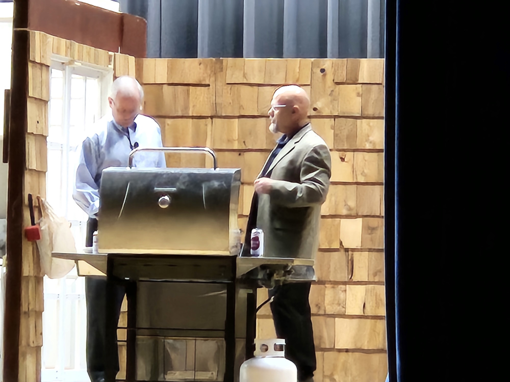 Two men standing and talking next to a barbecue grill.