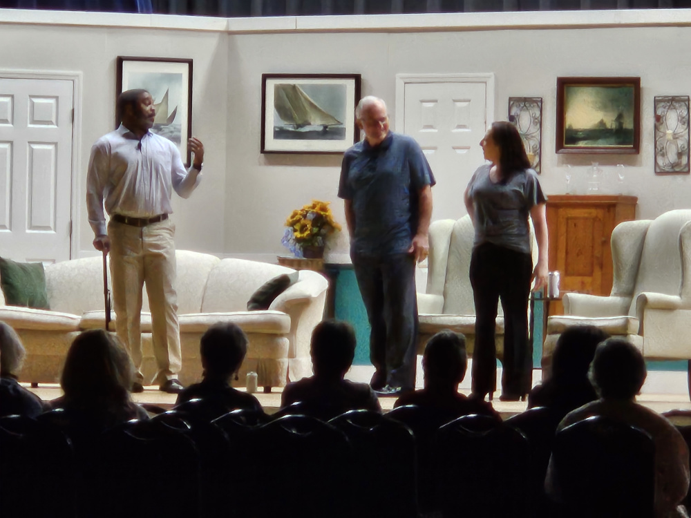 A man with a cane, a man in a blue T-shirt and a woman in gray top and black pants standing.