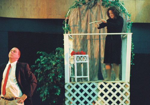 A woman on a balcony aiming a pop gun at a man below