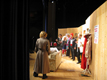 Woman in a raincoat and the cast standing along wall