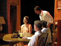 A man and two women sitting at a table with another standing man talking