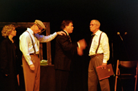 A man putting his hand on the shoulder of a man in a suit talking with a man with a moustache, while a woman looks
        on