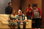 A man and a woman sit on a couch, while a man in a suit, a young woman, a man in a red Avengers
       T-shirt and a man in a Tampa Bay Buccaneers T-shirt look on behind them