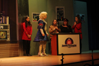 The man in the wig and white and blue sparkly skirt, the woman in the gold Starfleet uniform sitting at a console, the woman in the black sparkly skirt sitting
       at a console, with two women in red Starfleet uniforms on either side 