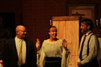 A bald man, a woman and a man in a suit in front of a tall wooden box