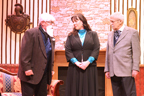 A man in a white beard talking to a woman in a dark gray dress with a blue blouse and Dr. Watson in a gray jacket and gray ascot