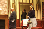 The bald man, the woman in the dark dress and the woman in the vertical gray striped dress standing