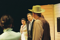 A man in a suit addresses a man in a cowboy hat while two women look on