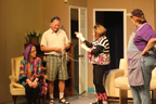 A woman wearing a rainbow-colored blouse, a man in green plaid shorts, a woman who thinks she's a cat, and a woman in an apron and baseball cap