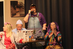 A woman in curlers, a man in a blue cap reading a book about cats, a woman wearing an apron and baseball cap talking on the phone, and a woman in a brightly-colored outfit praying