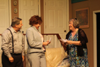 A man wearing black suspenders, a woman wearing a gray pantsuit, and a woman wearing a shawl