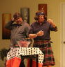 A man in a gray shirt and tie and a man in a kilt and headband