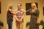 A young woman in jeans and sandals shakes hands with the woman in a horizontally
       striped long dress, with a young man in a plaid shirt behind them