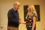 A man in a cardigan sweater shaking hands with a young woman in a floral print blouse