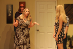 A woman in a dark dress with flower outlines gestures and talks to a young woman in a dark floral print dress