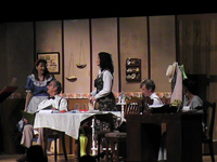 Two woman standing, two men and one woman sitting at a table