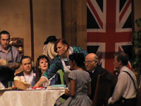 Family sitting at a table with standing woman reaching across