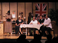 Three men and a woman at a table, and one woman standing