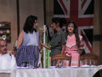 Three woman standing behind a table with one man sitting